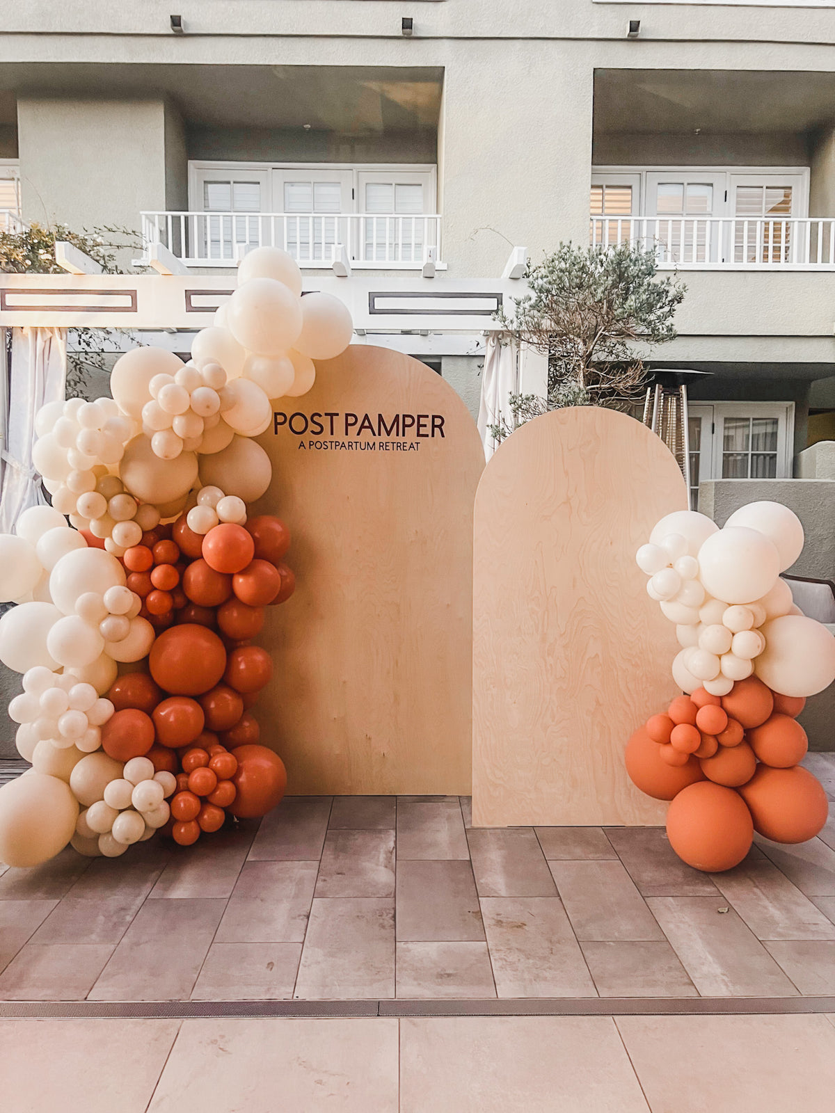 Terracotta and cream balloon garland framing wooden arch backdrops for a brand event
